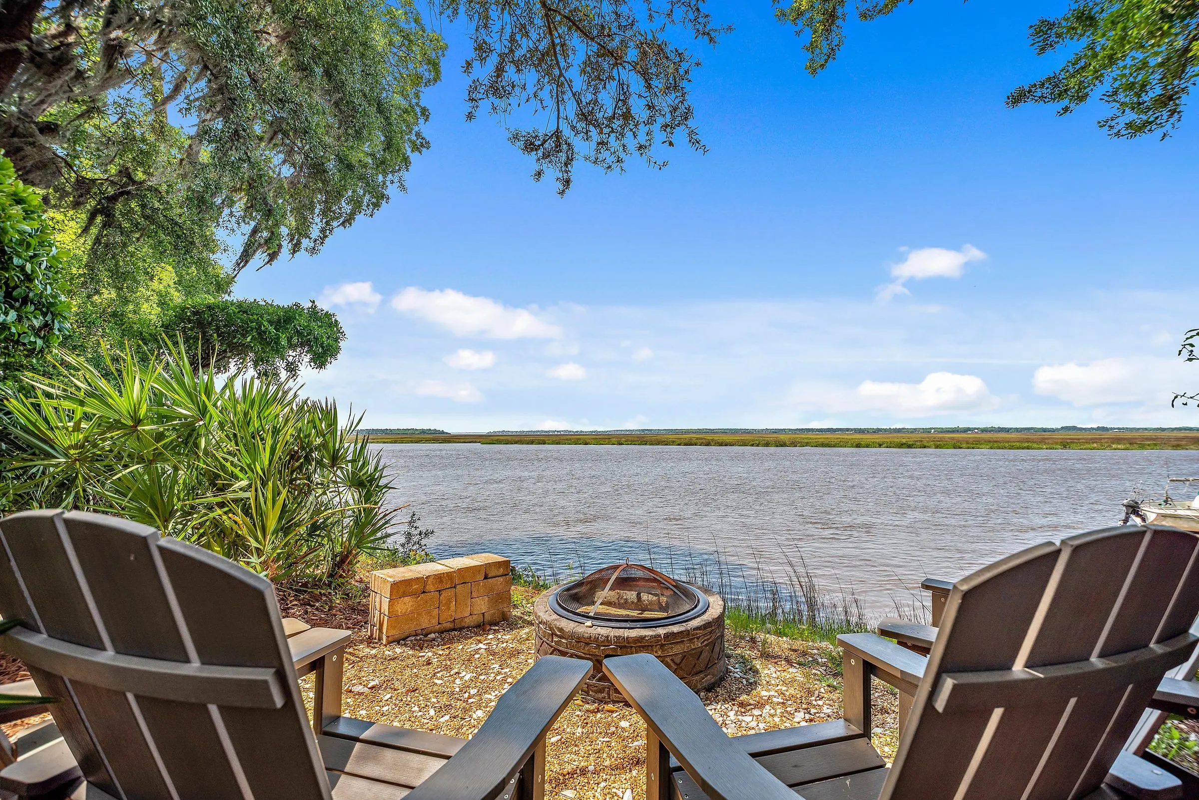 Waterfront deck with Adirondack chairs and a fire pit, looking toward the marsh